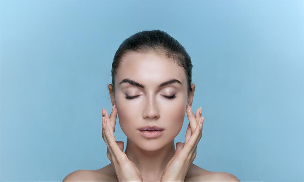 Woman touching her face against a light blue background